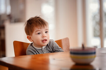 Little emotional toddler boy sitting at a wooden table with deep plate