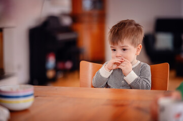 Little toddler boy sitting at wooden table sadly looking sideways