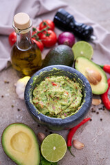 freshly made guacamole in marble mortar with ingredients on grey concrete background