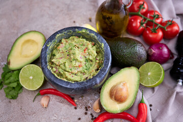 freshly made guacamole in marble mortar with ingredients on grey concrete background