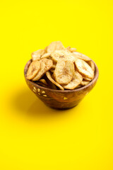 banana chips in wooden bowl on yellow background.