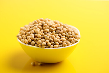 Dry soybean seed in bowl on yellow background.