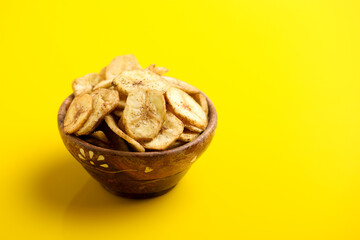 banana chips in wooden bowl on yellow background.