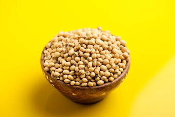 Dry soybean seed in wooden bowl on yellow background.