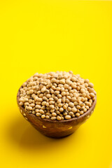 Dry soybean seed in wooden bowl on yellow background.