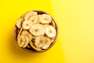 banana chips in wooden bowl on yellow background.