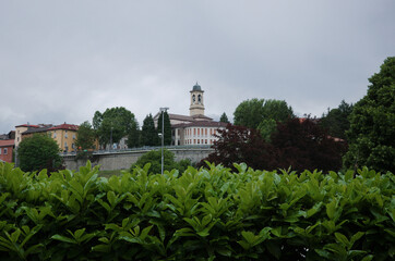 View of bell tower of Parrocchia Sant Antonino church in Borgo Val di Taro town, Parma Province, Italy. View through lush foliage to Via lungo Taro Brigate Julia Street and old town wall of Borgotaro