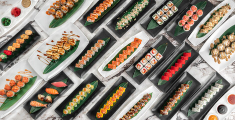 banner with different sets of maki sushi rolls, nigiri and gunkan with tiger shrimp, tomago, salmon, tuna, chuka salad, tuna and bamboo leafs in a white and black plates above a marble table, top view © Alexander