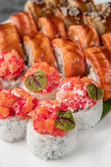 set of different colorful maki sushi rolls with tuna, salmon, shrimp, crab and avocado and green bamboo leaf in a white ceramic plate with chopstick, side view, close-up