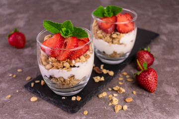 Strawberry parfait in a glass with yogurt and granola on a gray background.	