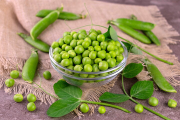 Green peas in a glass bowl on a gray table.
