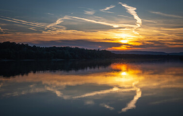 Sunset in nature. Spectacular sunset on the river bank. Reflection of clouds and lights in the water.