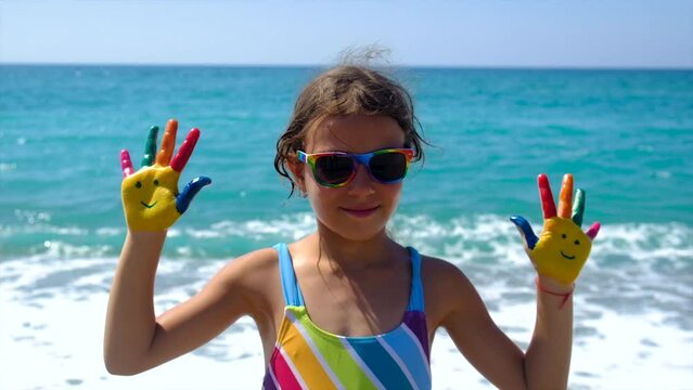 A child at the sea with paints on her hands a smile. Selective focus.