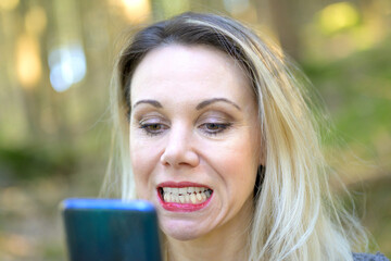 Blond woman examining her teeth in a hand mirror