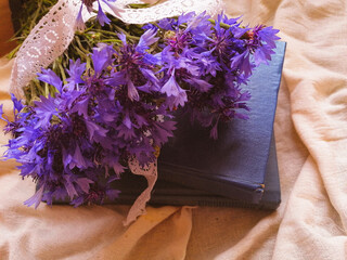 bouquet of purple cornflowers with white vintage ribbon with blue books top view