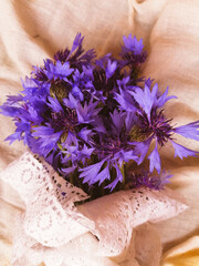 bouquet of purple cornflowers with white vintage ribbon on the table at sunset
