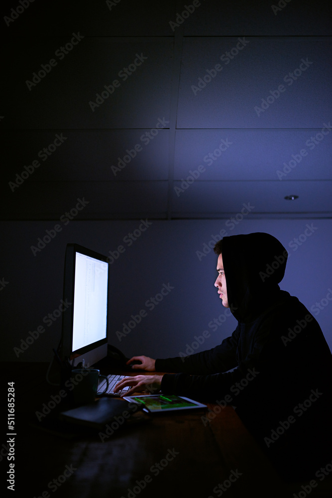Poster scouring the net for his next victim. shot of a hooded computer hacker using a computer in the dark.