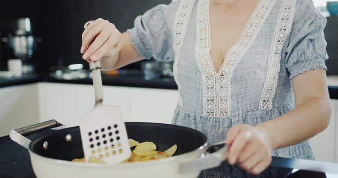 Side view: Attractive young woman fries potatoes on a modern electric stove with a built-in extractor fan