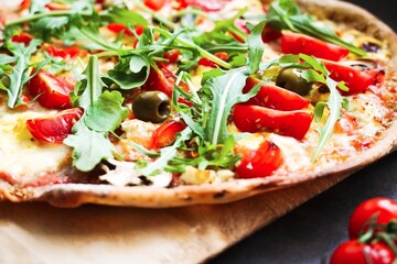 Freshly baked pizza with arugula, tomato, olive, mushrooms, sweet pepper, hollandaise sauce and mozzarella