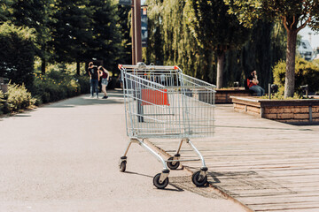 An abandoned shopping cart on a public park alley. Forgotten trolley outside a mall or supermarket.
