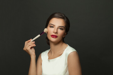 Obraz premium Beauty Face. Portrait of beautiful model applying blush with cosmetic brush. Young woman with soft smooth skin and fresh makeup. Skin cosmetics.