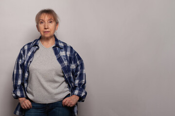 Middle age senior woman in grey t-shirt standing against grey studio wall background