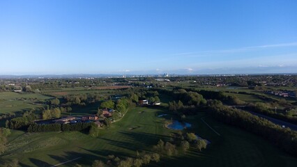 Fototapeta na wymiar Aerial view looking down onto a golf course surrounded by green fields with the Manchester skyline in the distance. 