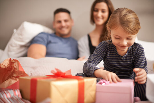 I wonder what it could be.... Shot of a little girl receiving presents in bed from her parents.