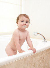 Bath time is over. An adorable baby girl climbing out of the bath.