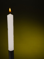glowing whole white candle on a dark yellow background