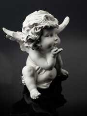plaster white statuette in the form of an angel on a black background with reflection