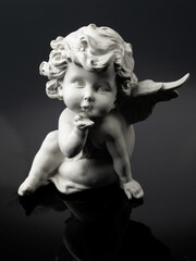 plaster white statuette in the form of an angel on a black background with reflection