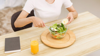 Lifestyle in living room concept, Young Asian woman mixing vegetable salad with salad dressing