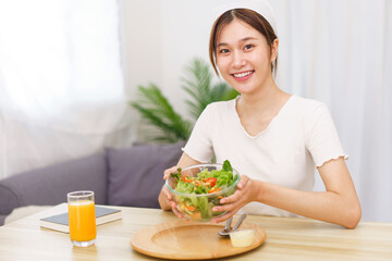 Obraz na płótnie Canvas Lifestyle in living room concept, Young Asian woman smiling and holding bowl of vegetable salad