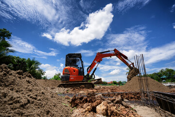 An orange mini excavator is digging sand at the construction site.