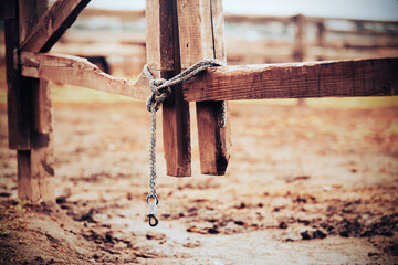 The bottom of an old wooden paddock gate on a farm, closed on a lead rope, knotted on a cloudy day. An empty paddock for domestic cattle. Rural area.