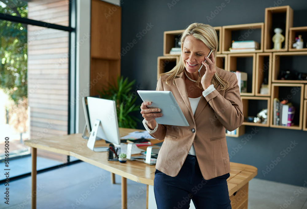 Poster Merging tech with success. Shot of a mature businesswoman using a digital tablet while talking on a cellphone in an office.