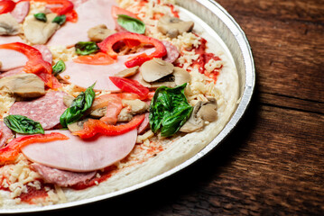 Fototapeta na wymiar Pizza edge closeup on a wooden background. Bacon, salami, mushrooms and greens.