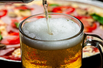 A glass in which beer is poured close-up on a background of pizza.