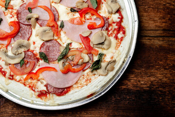 Pizza edge closeup on a wooden background. Bacon, salami, mushrooms and greens.