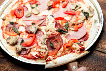 Pizza edge closeup on a wooden background. Bacon, salami, mushrooms and greens.