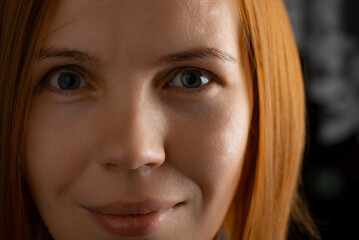 The face of a red-haired woman of middle age 40 years old close-up. She looks into the camera.