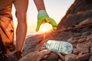 Earth Day. Volunteer picks up a plastic bottle on the beach. Close up of hand. The concept of...