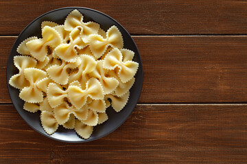 Farfalle, cooked pasta, on dark plate, on wooden brown plank tabletop background, top view, space to copy text..
