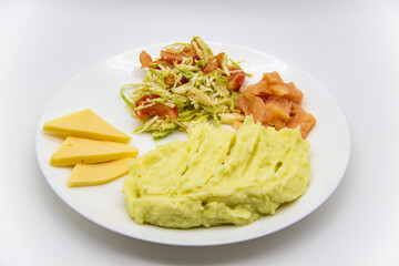 Tasty breakfast or lunch with potato puree with fresh salad with cabbage and tomatoes, cucumber and red fish - salmon, and pieces of cheese on the white plate