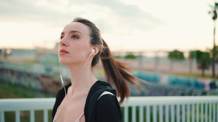 Young woman with freckles and long ponytail wearing black sports hoodie in wired headphones listens...