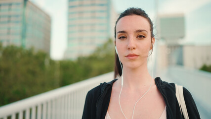 Young woman with freckles and long ponytail wearing black sports hoodie in wired headphones listens...