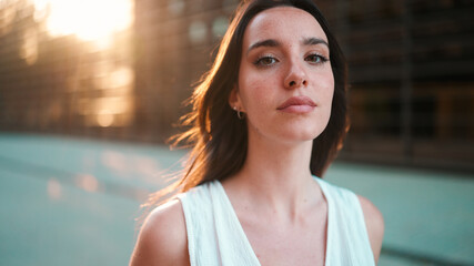 Close-up portrait of young woman with freckles and dark loose hair and long eyelashes wearing white...