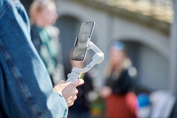 Blogger filming outdoor event on smartphone with gimbal stabilizer, video blogging for new followers