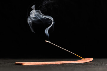 Smoke curls of burning incense stick in wooden holder for relaxation and meditation black background